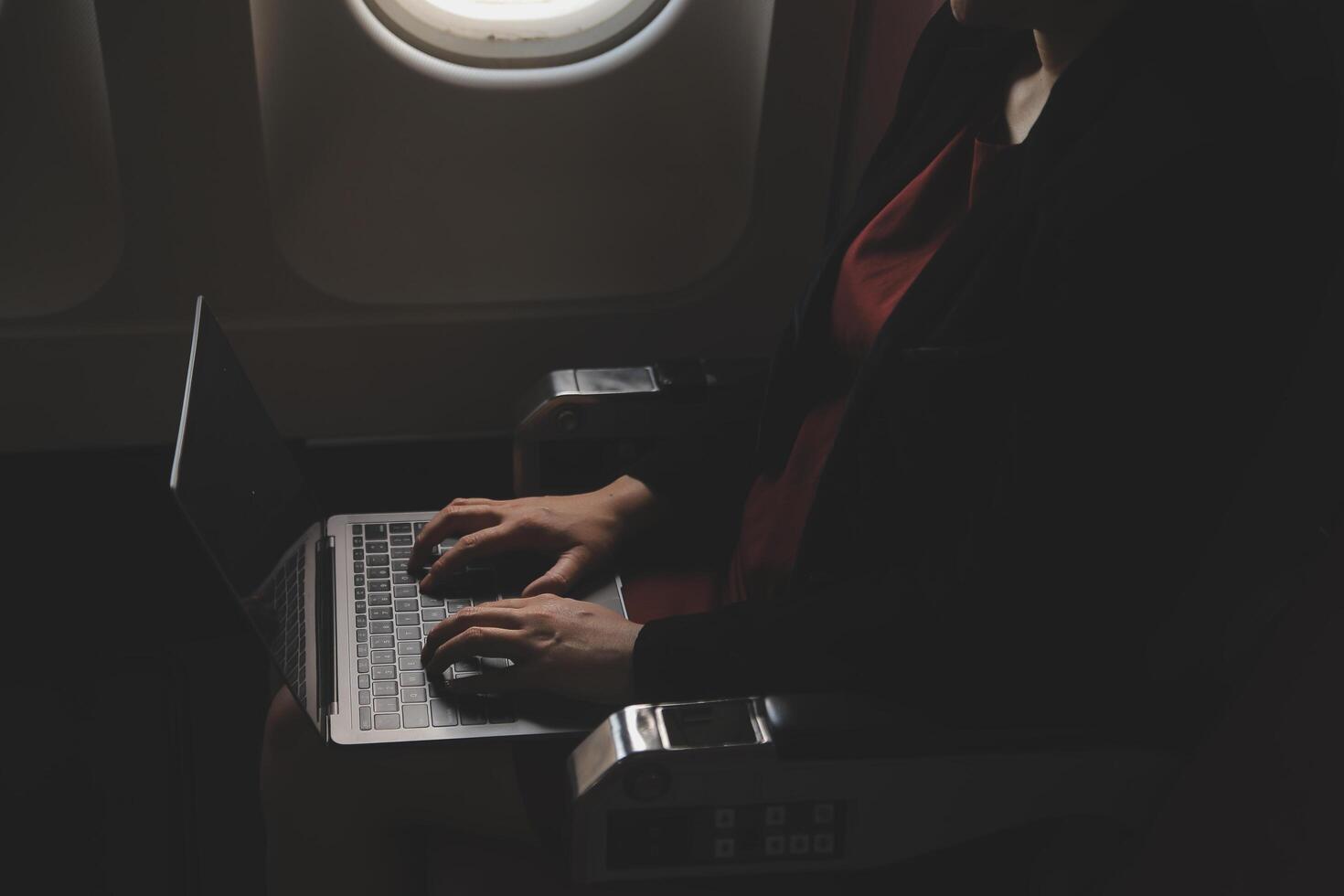 Blonde female tourist checking incoming notification on smartphone sitting on seat of airplane with netbook.Young businesswoman share media from telephone on laptop computer during plane flight photo