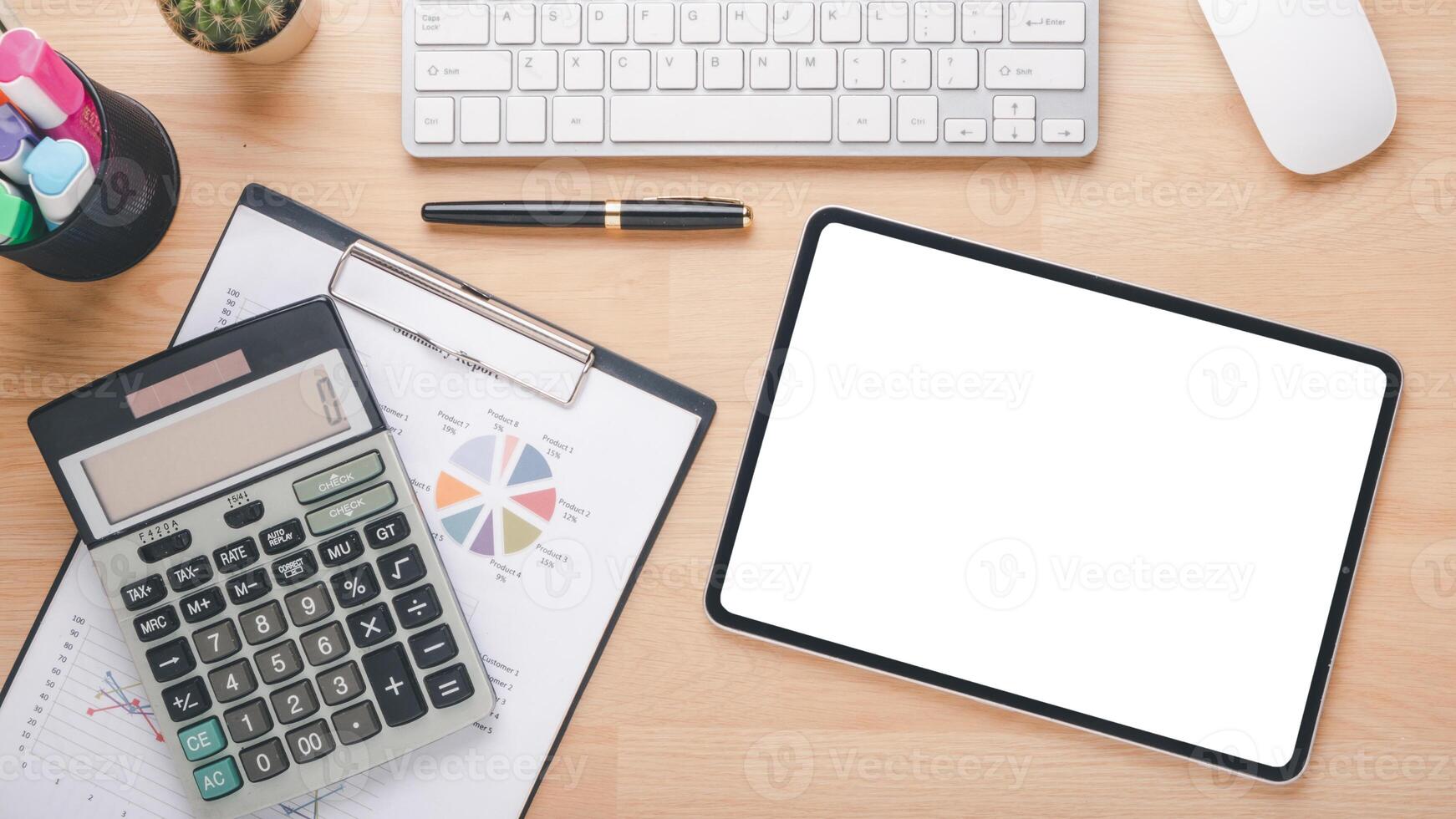 A professional business analytics workspace with a blank tablet screen, calculator, clipboard with charts, and a white keyboard on a wooden desk. photo