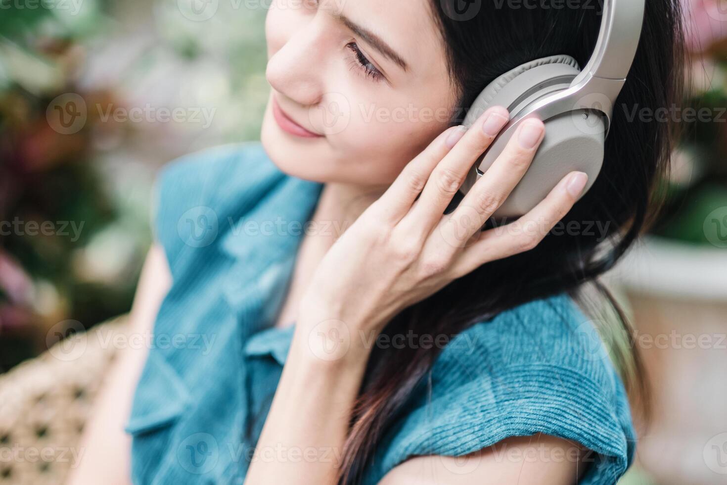 A close up of a serene woman adjusting her headphones, immersed in the soundscape of her tranquil garden environment. photo