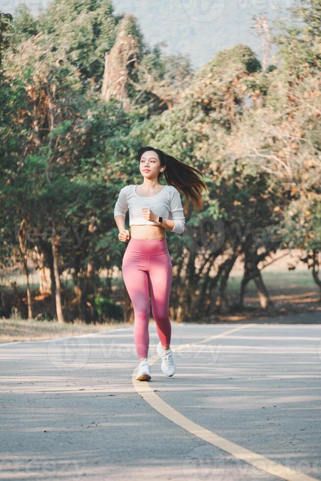 A joyful runner wearing pink leggings and white sneakers exudes happiness and health while jogging on a park path, surrounded by greenery. photo