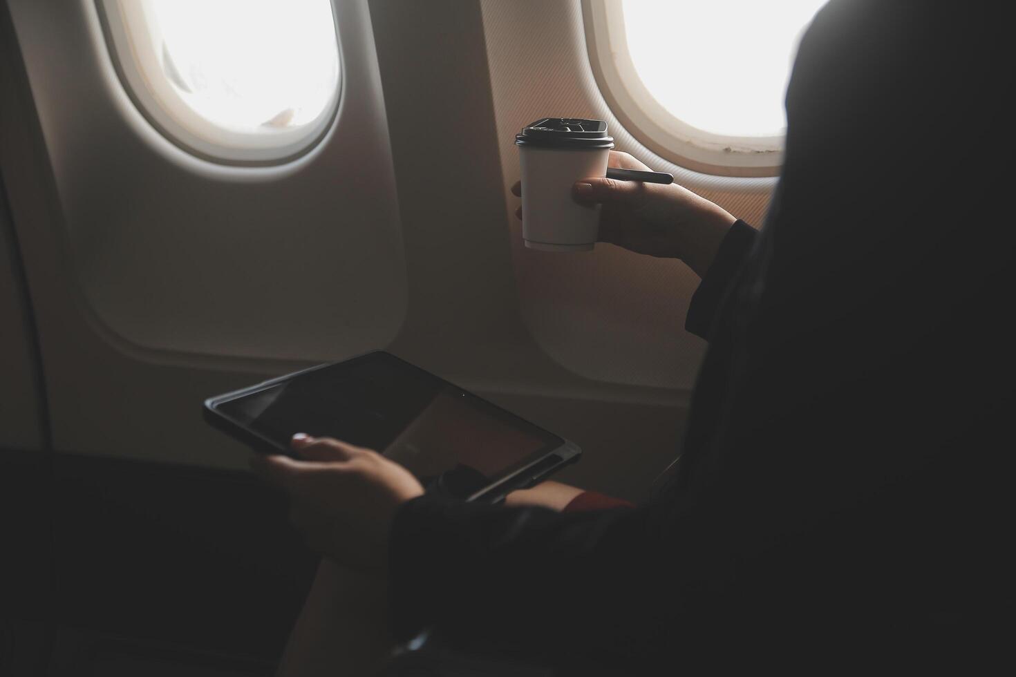 Blonde female tourist checking incoming notification on smartphone sitting on seat of airplane with netbook.Young businesswoman share media from telephone on laptop computer during plane flight photo