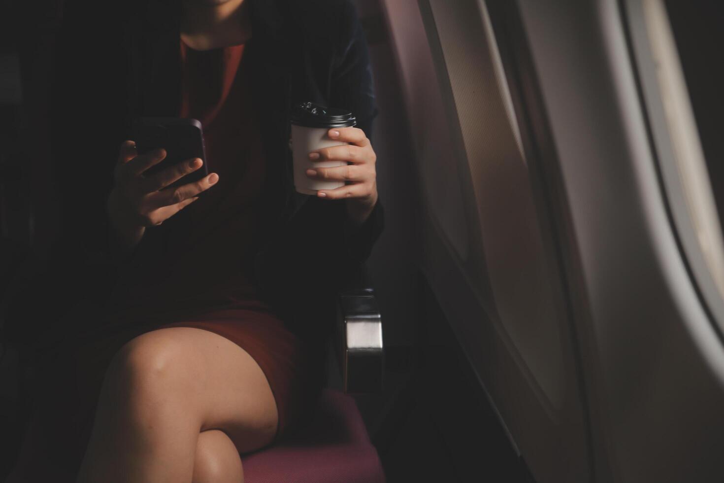 Blonde female tourist checking incoming notification on smartphone sitting on seat of airplane with netbook.Young businesswoman share media from telephone on laptop computer during plane flight photo