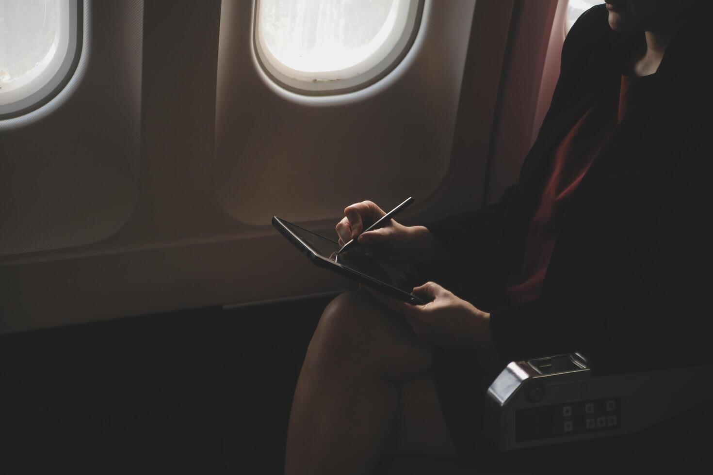 Blonde female tourist checking incoming notification on smartphone sitting on seat of airplane with netbook.Young businesswoman share media from telephone on laptop computer during plane flight photo