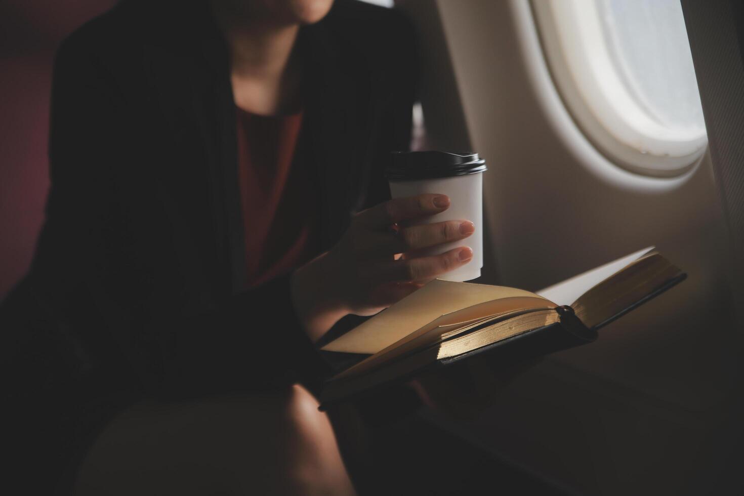 Blonde female tourist checking incoming notification on smartphone sitting on seat of airplane with netbook.Young businesswoman share media from telephone on laptop computer during plane flight photo