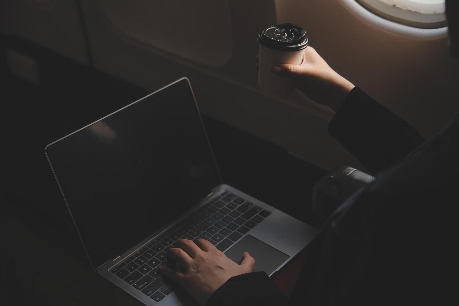 Blonde female tourist checking incoming notification on smartphone sitting on seat of airplane with netbook.Young businesswoman share media from telephone on laptop computer during plane flight photo