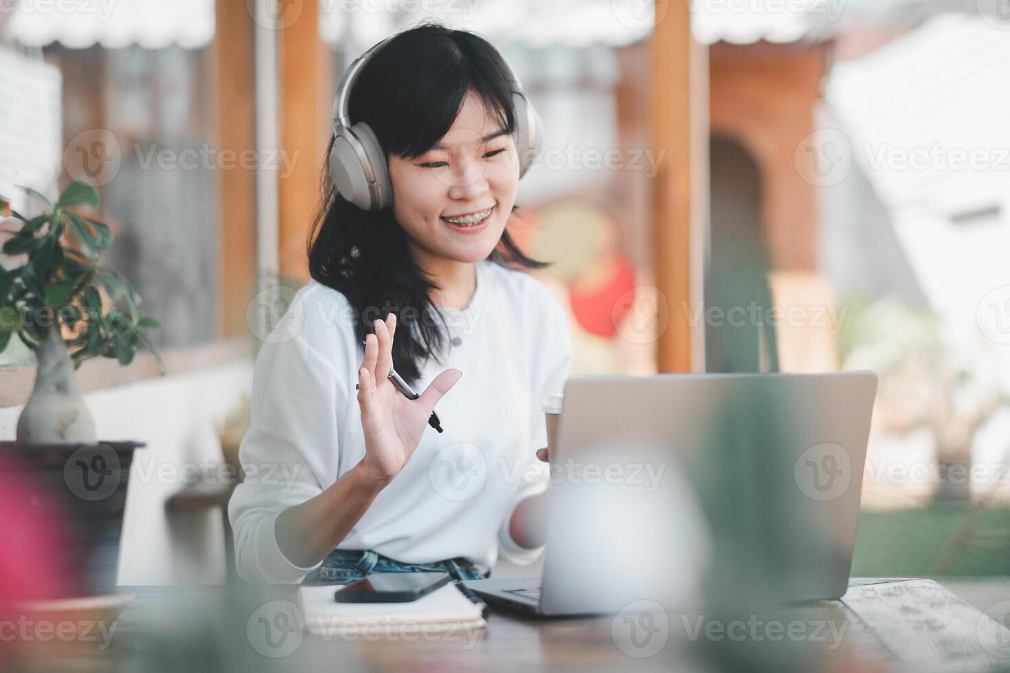 A smiling young woman engages in an animated conversation on a video call, wearing headphones, and using a laptop at a home environment, showcasing remote communication. photo