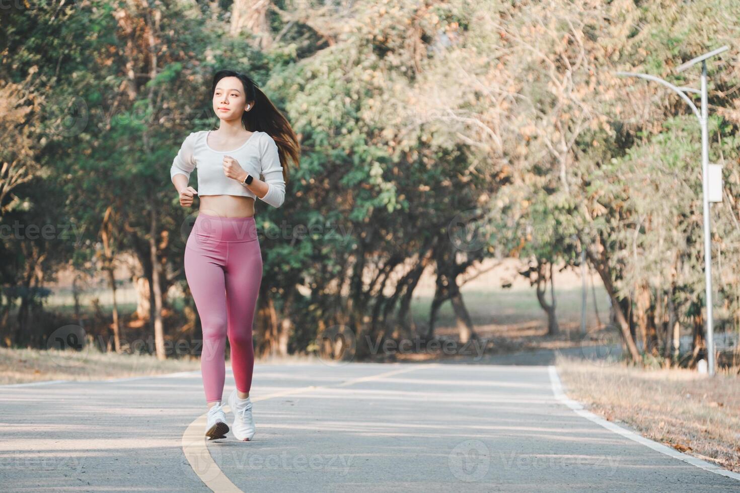 A joyful runner wearing pink leggings and white sneakers exudes happiness and health while jogging on a park path, surrounded by greenery. photo