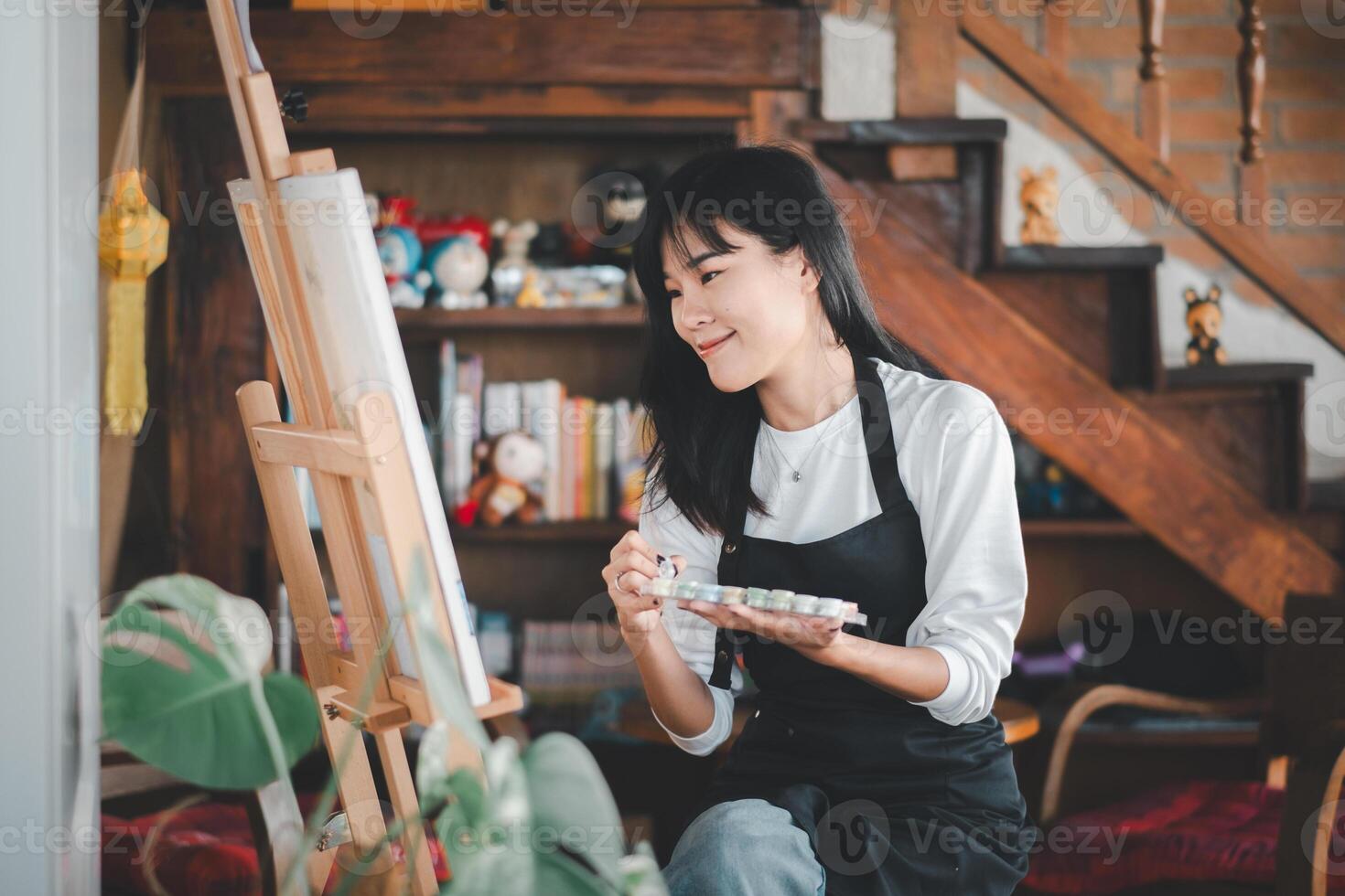 An aspiring artist with a serene expression delicately applies brush strokes to a canvas in a cozy, well-decorated studio filled with creative inspiration. photo