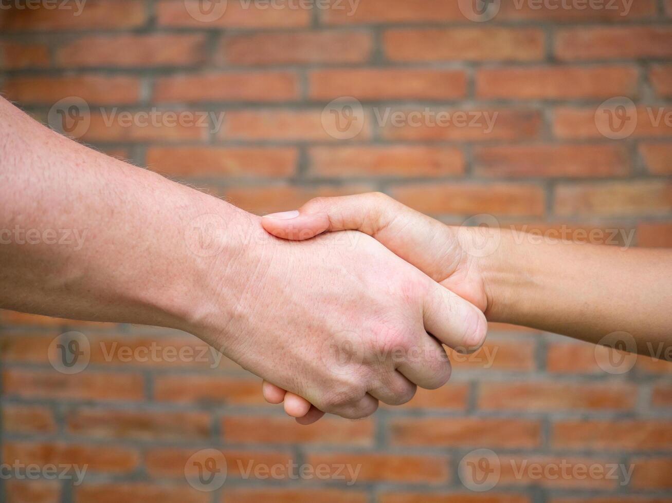 Close-up of shaking hands between man and woman with a brick background. Concept of partnership and teamwork photo