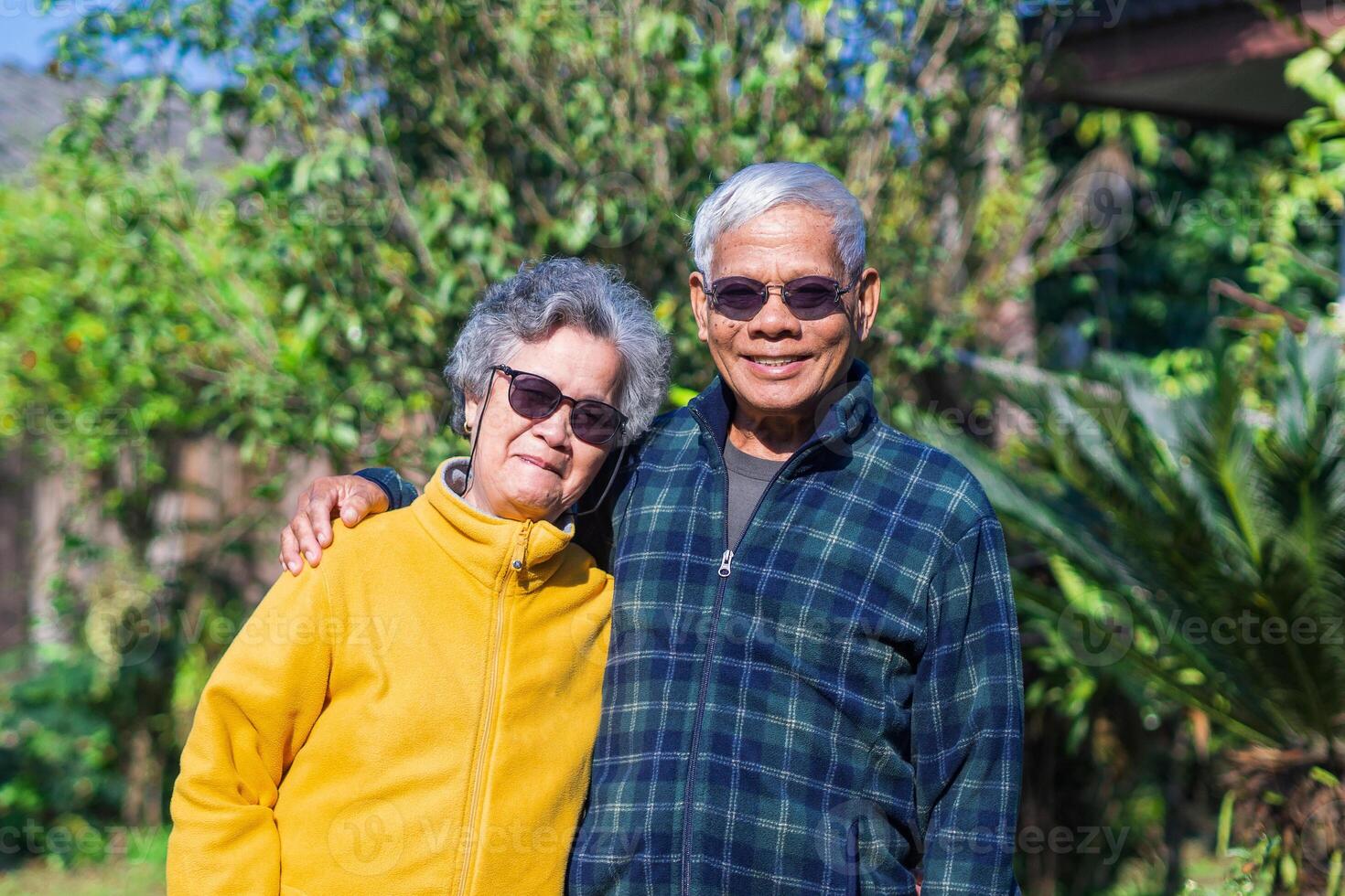 Portrait of an elderly couple wearing sunglasses smiling and looking at the camera while standing in a garden. Space for text. Concept of aged people and healthcare photo