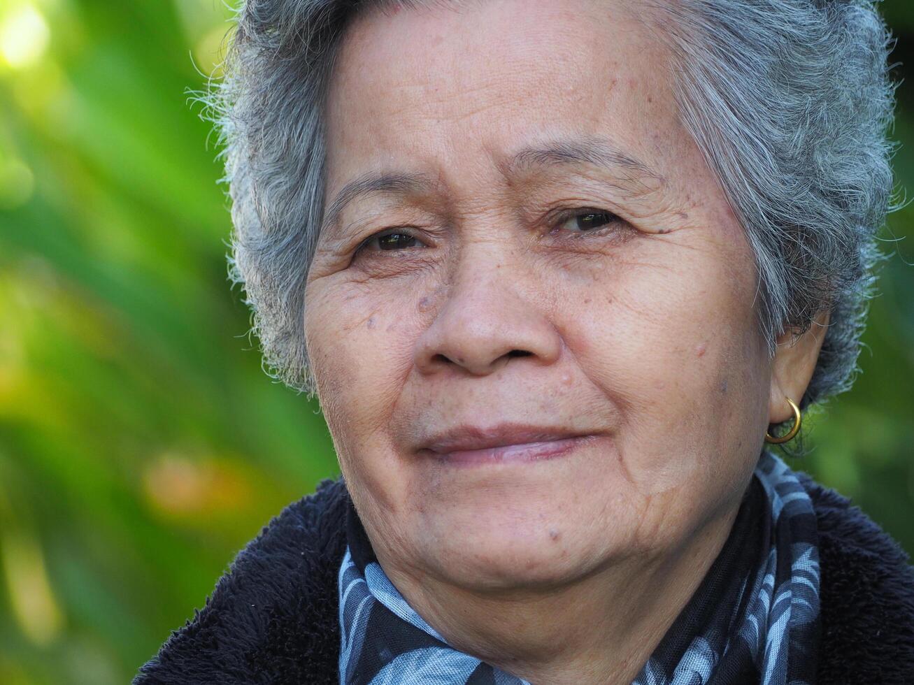 Senior Asian woman with short white hair smiling and looking at the camera while standing in a garden. Space for text. Concept of aged people and healthcare photo