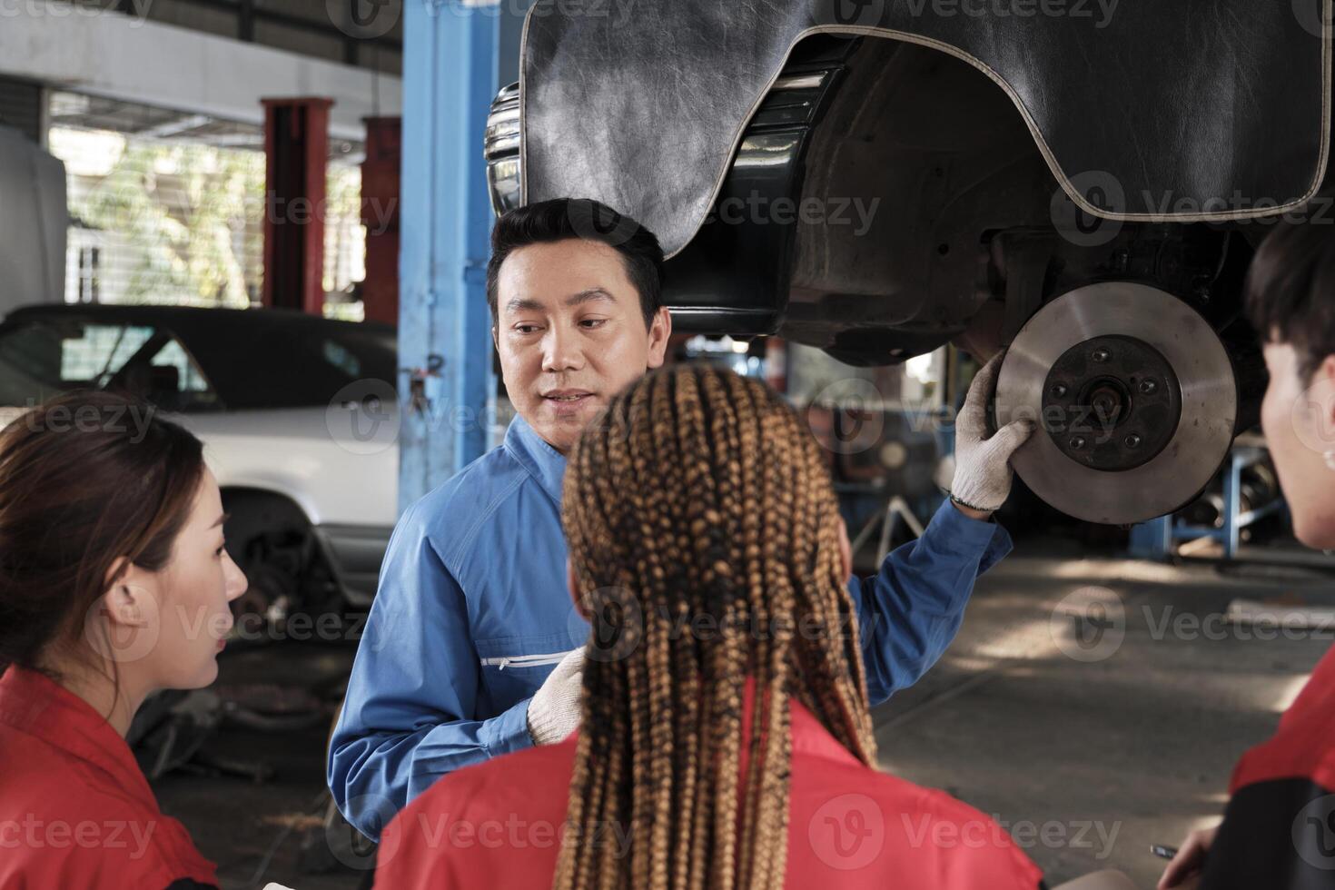 asiático masculino profesional automotor ingeniero supervisor describe coche rueda y suspensión reparar trabajo con mecánico trabajador personal equipo en reparar Servicio cochera, especialista ocupaciones en auto industria. foto
