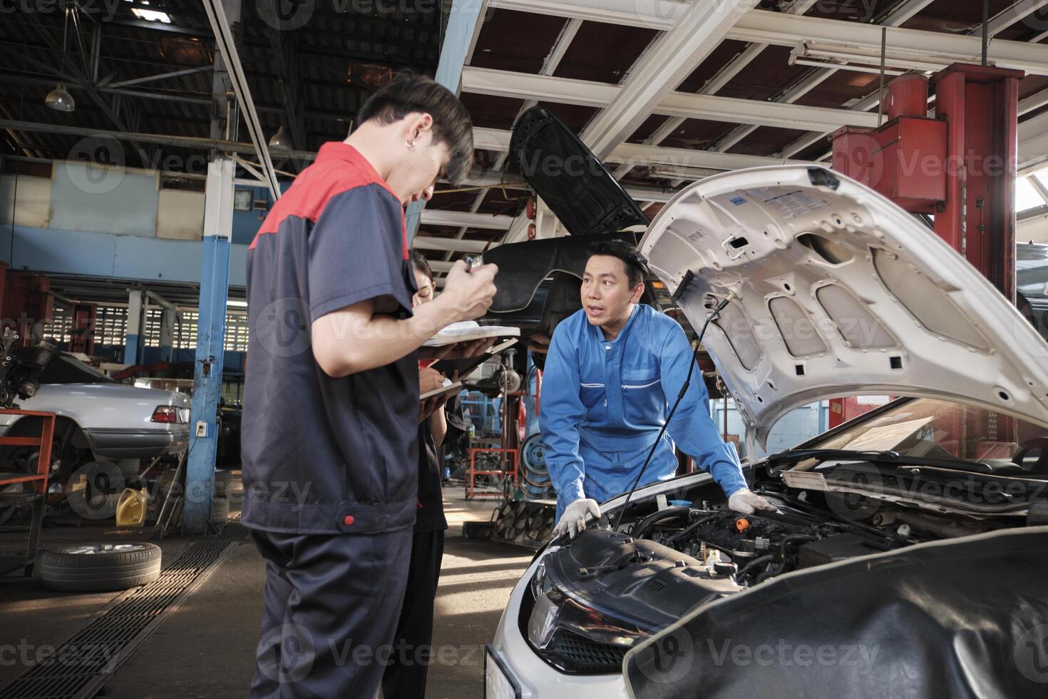 Asian male professional automotive engineer supervisor describes car engine maintenance and repair work with mechanic worker staffs team in fix service garage, specialist occupations in auto industry. photo
