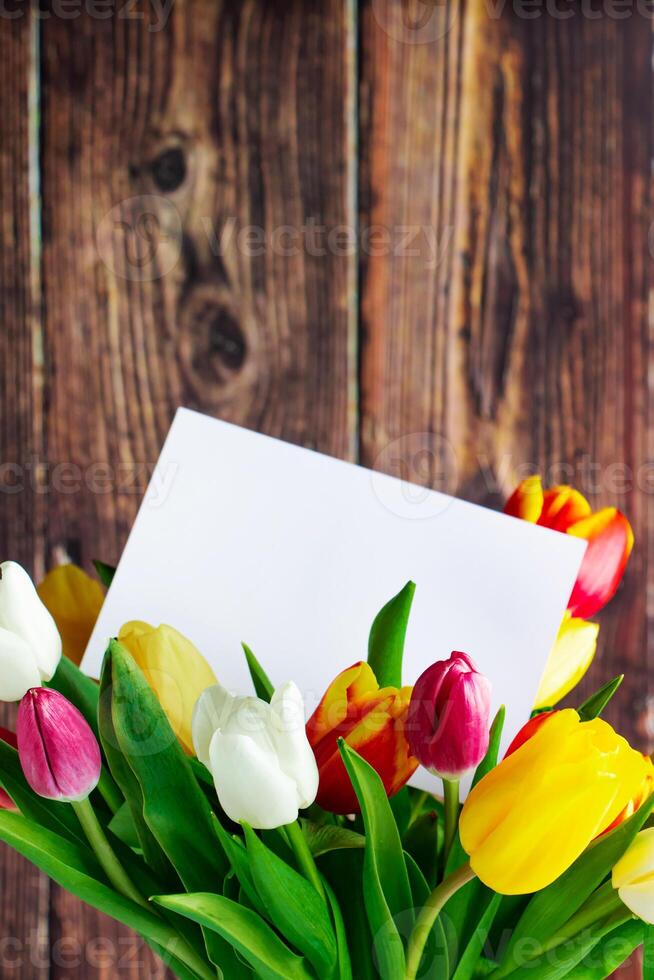 Colorful tulips bouquet and greeting card on wooden background. Holiday gift. photo