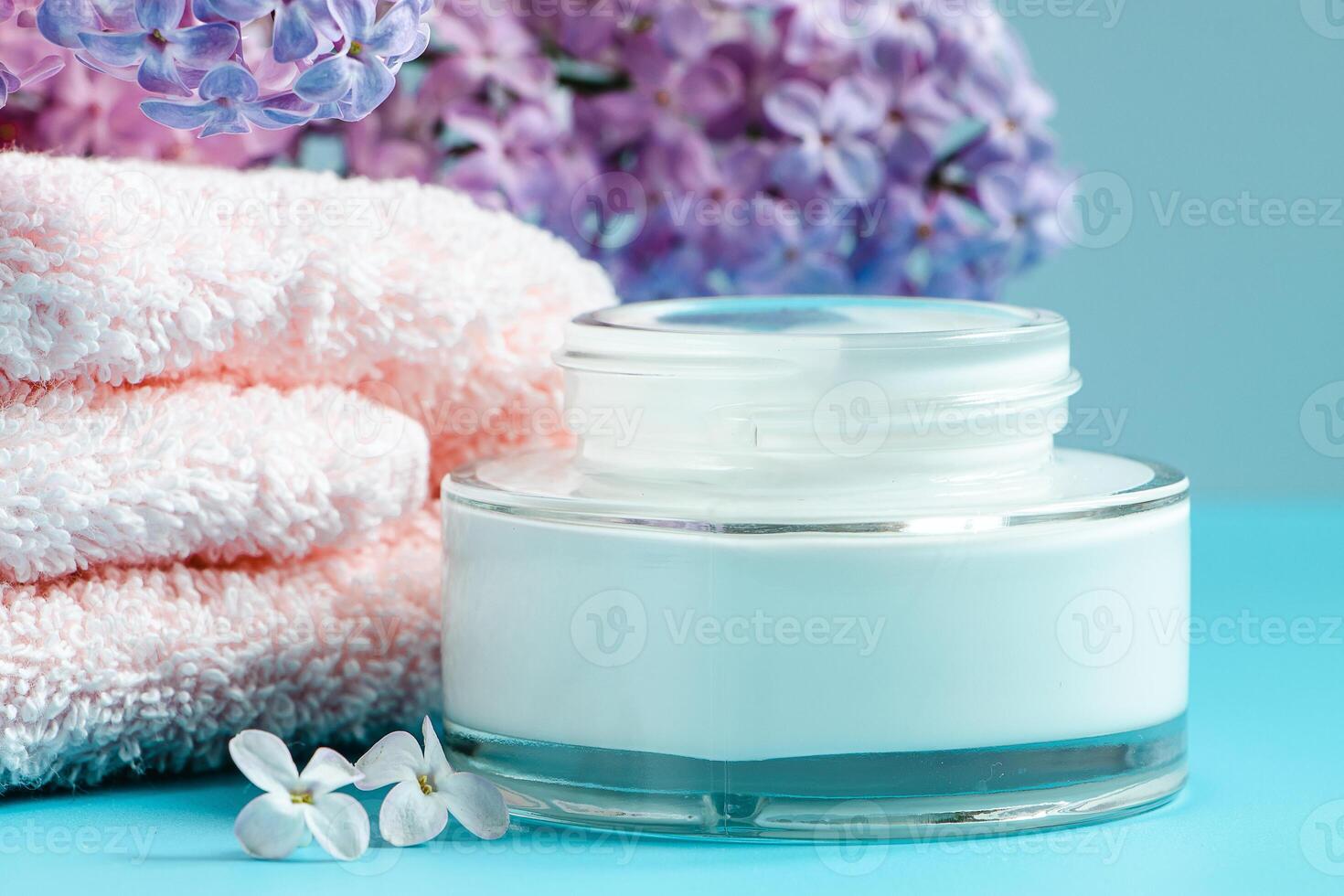 Towel, cream and soap on background of delicate lilac flowers. photo