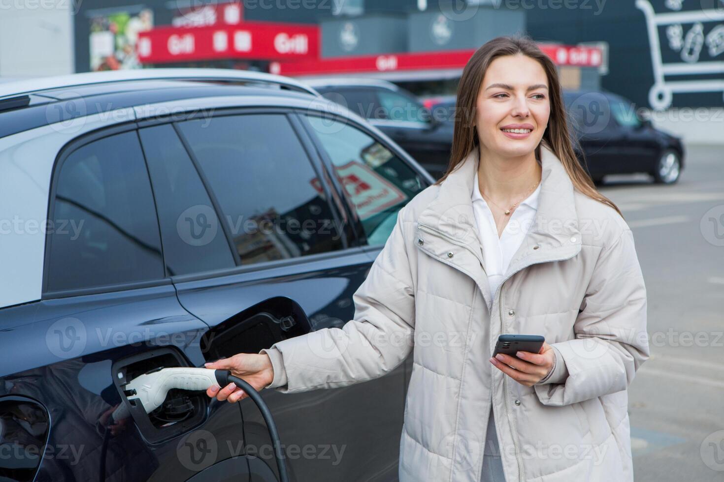 Young woman charging her electric car at a charging station in the city. Eco fuel concept. The concept of environmentally friendly transport. Recharging battery from charging station. photo