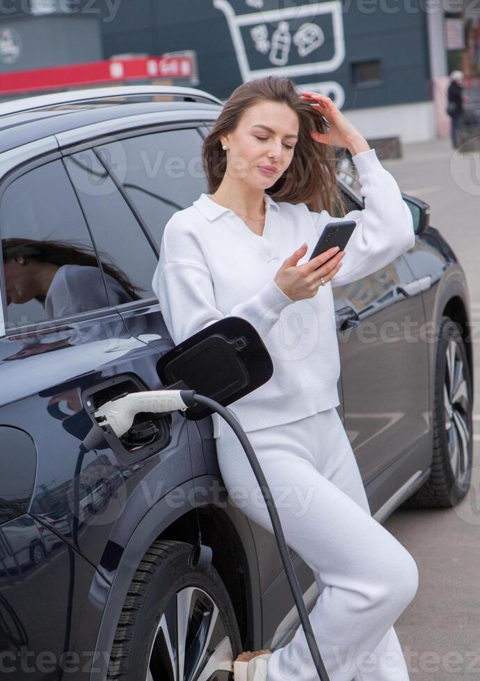 Young woman charging her electric car at a charging station in the city. Eco fuel concept. The concept of environmentally friendly transport. Recharging battery from charging station. photo