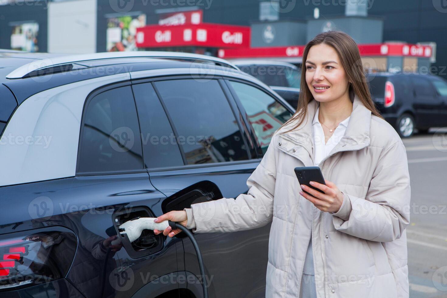 Young woman charging her electric car at a charging station in the city. Eco fuel concept. The concept of environmentally friendly transport. Recharging battery from charging station. photo