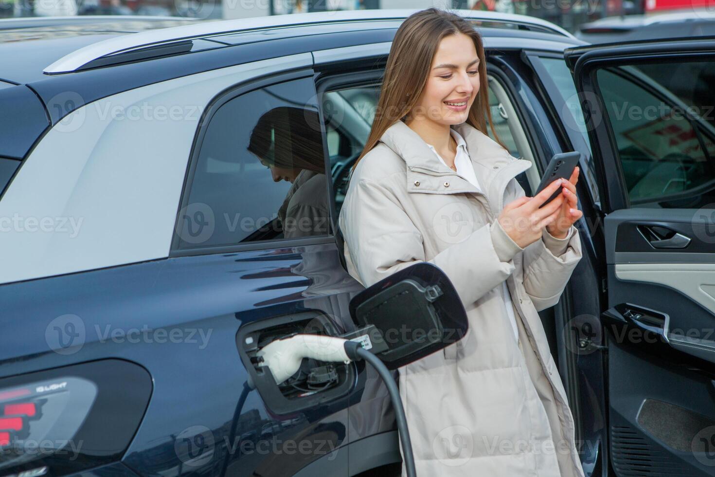 Young business woman refueling her electric car at a EV charging station. Concept of environmentally friendly vehicle. Electric car concept. Green travelling. photo