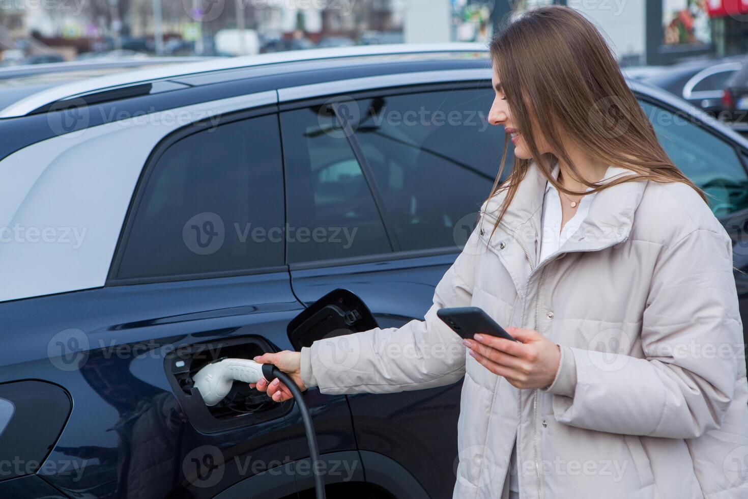 Young woman charging her electric car at a charging station in the city. Eco fuel concept. The concept of environmentally friendly transport. Recharging battery from charging station. photo