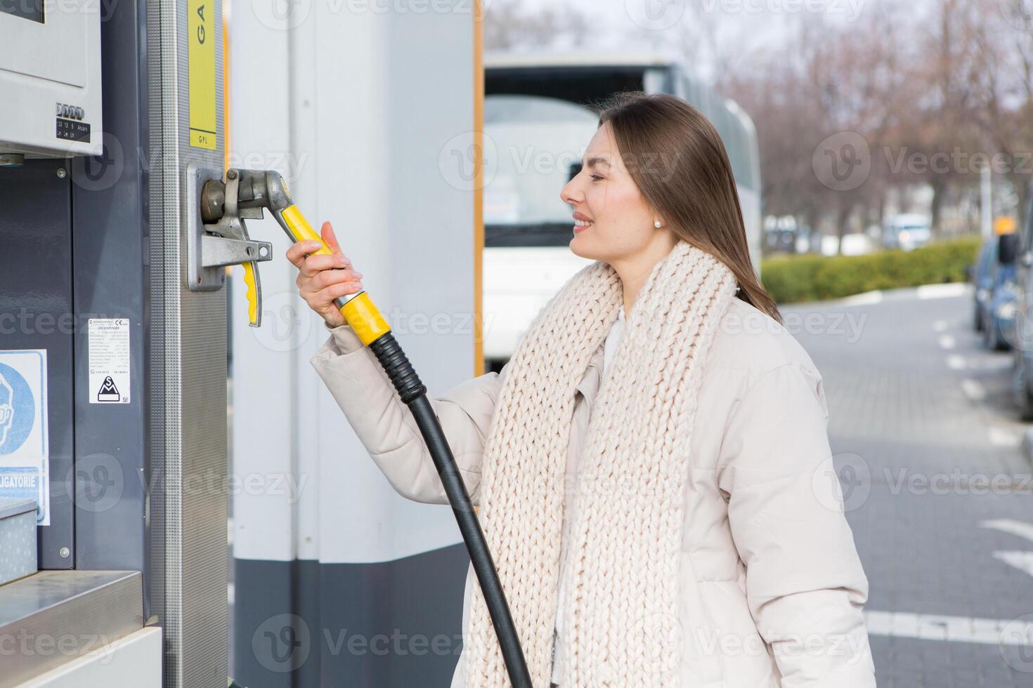 Young woman holding a fuel nozzle in her hand while refueling car at gas station. A stop for refueling at the gas station. Fueling the car with gas. photo