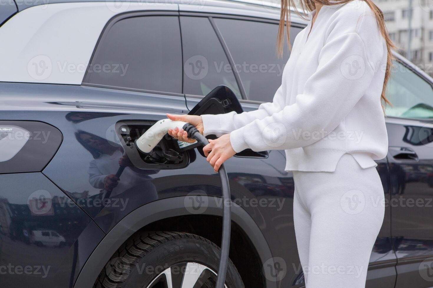 Young woman charging her electric car at a charging station in the city. Eco fuel concept. The concept of environmentally friendly transport. Recharging battery from charging station. photo