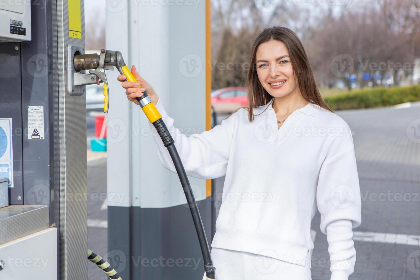 Young woman holding a fuel nozzle in her hand while refueling car at gas station. A stop for refueling at the gas station. Fueling the car with gas. photo