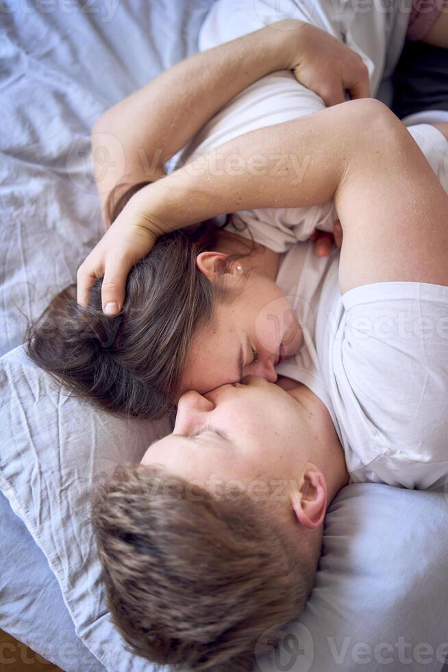 a young couple is lying on the bed, the girl is on the boy's shoulder, tender hugs photo