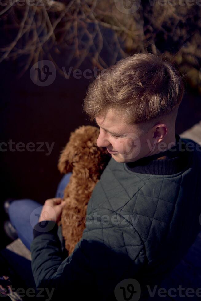 a boy sits on a pier and hugs a cockapoo photo