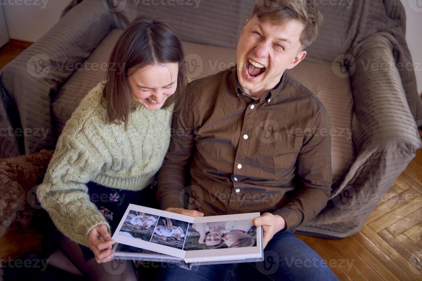 young couple looking at their wedding photo album by the bed in living room, cockapoo running around
