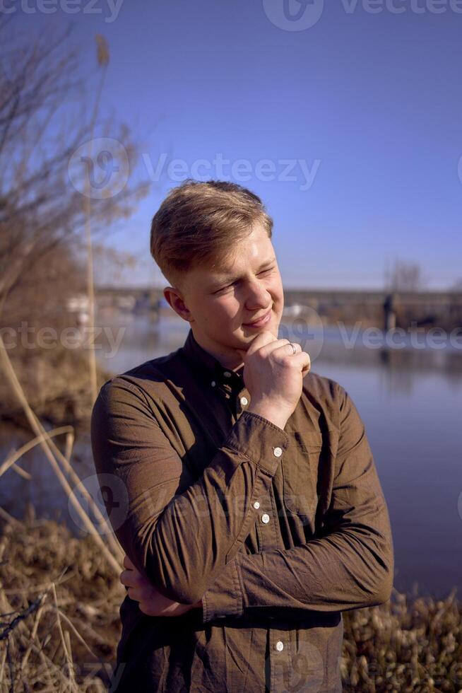 retrato de un joven hombre en un marrón camisa en el banco de un primavera río foto