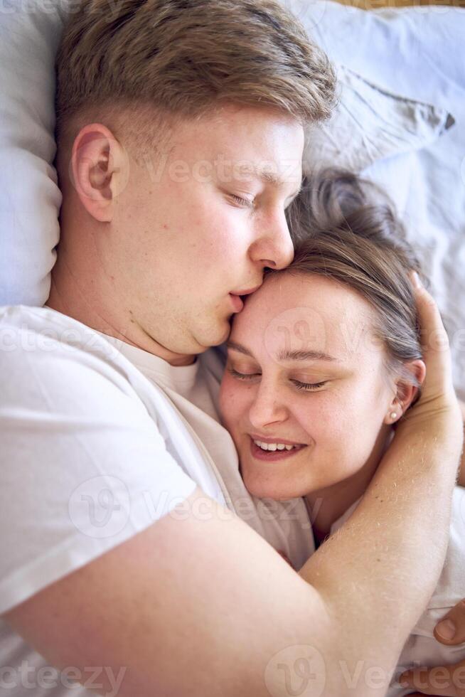 a young couple is lying on the bed, the girl is on the boy's shoulder, tender hugs photo