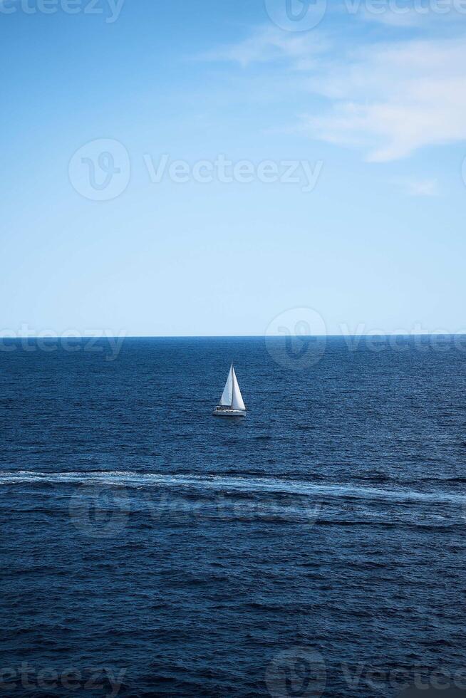 a lone white sailboat surrounded by deep blue water and a clear blue sky photo