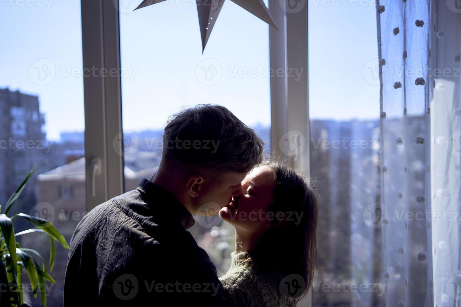 hermosa joven Pareja besos en el iluminar desde el fondo en contra el ventana foto