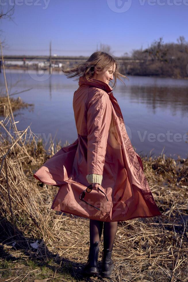 un elegante joven mujer en un rosado zanja bailes en el banco de un primavera río foto