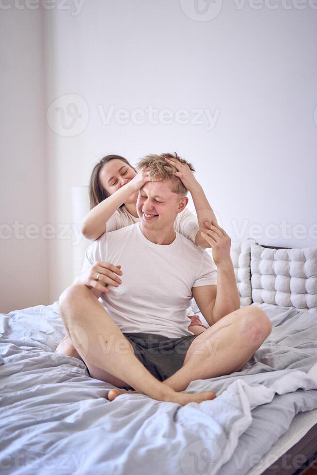 young couple on the bed, the woman combs the man's hair photo