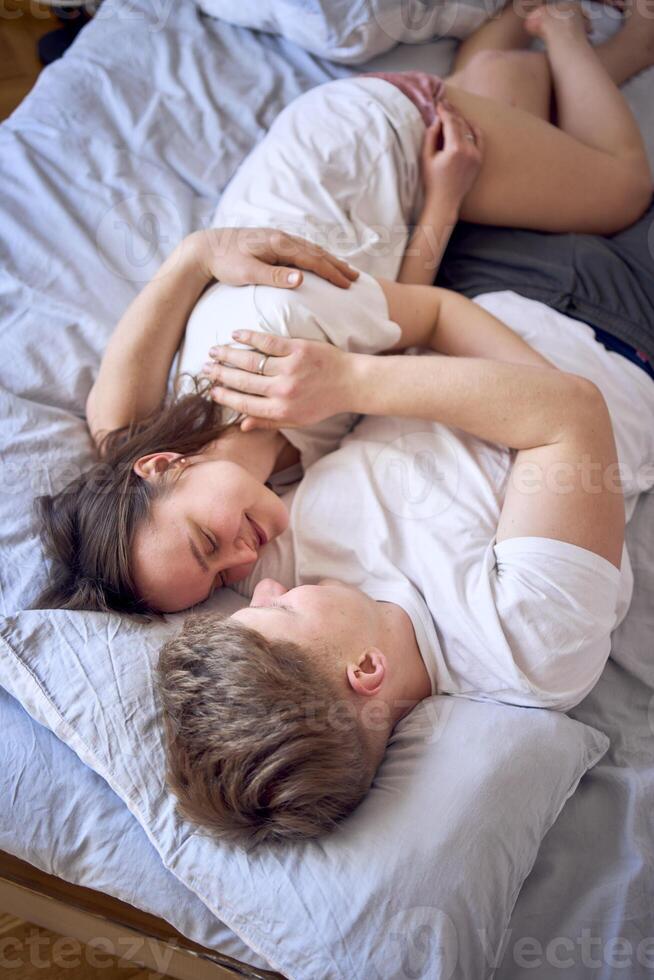 a young couple is lying on the bed, the girl is on the boy's shoulder, tender hugs photo