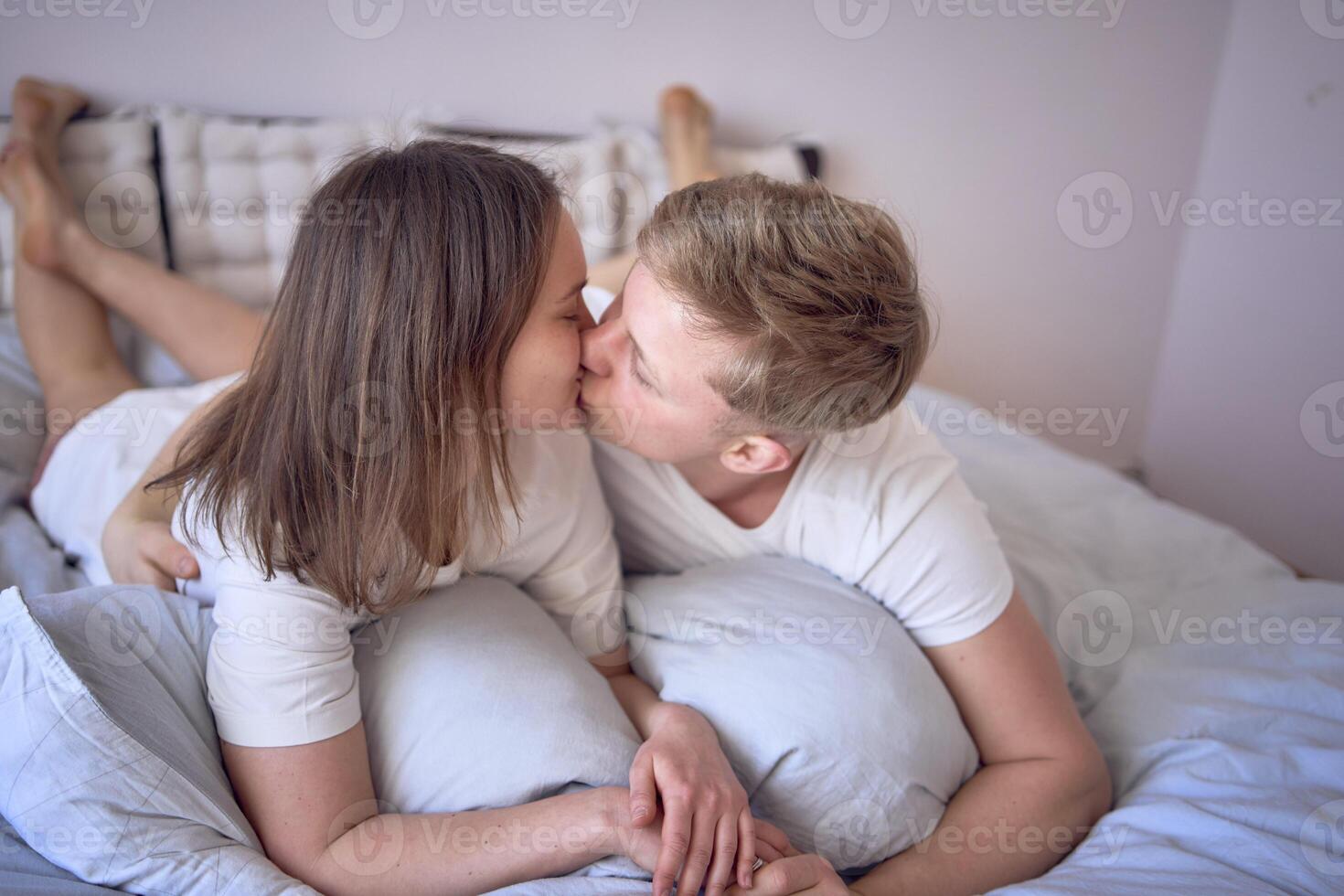 un joven hermosa Pareja abrazando y besos en cama, bienestar a hogar foto