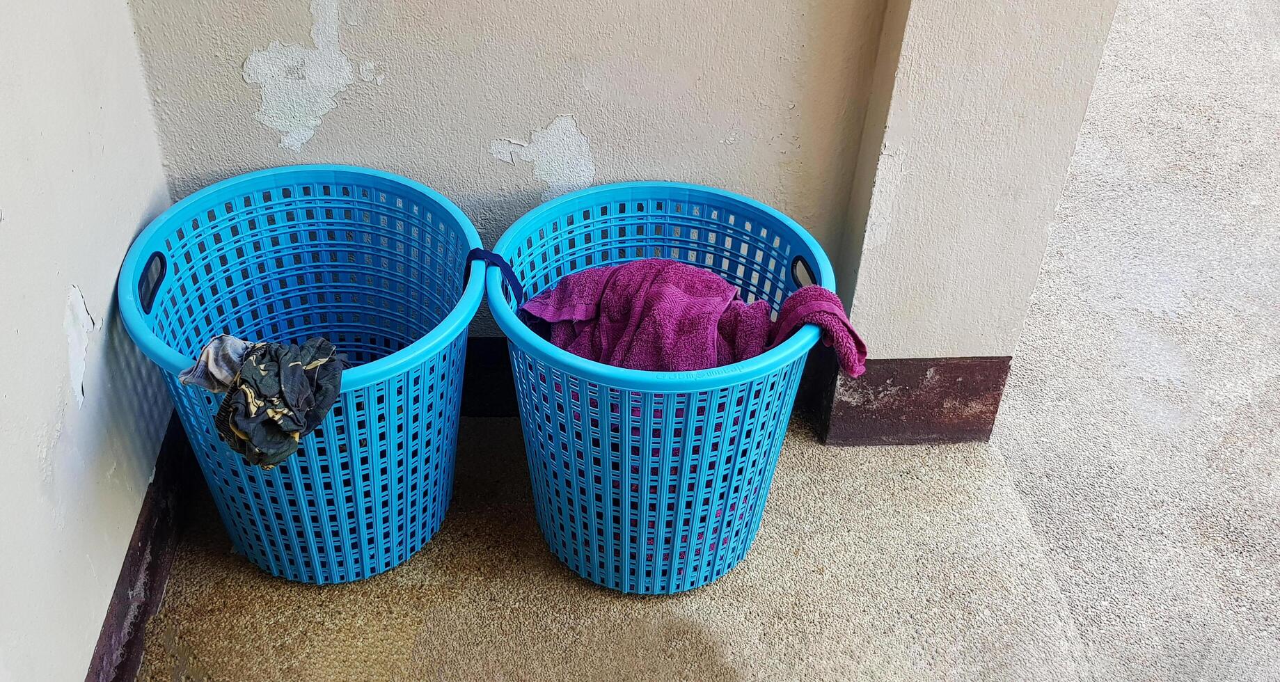 Two blue plastic baskets of used laundry put in corners of the room with copy space. Object with craked concrete wall background. photo
