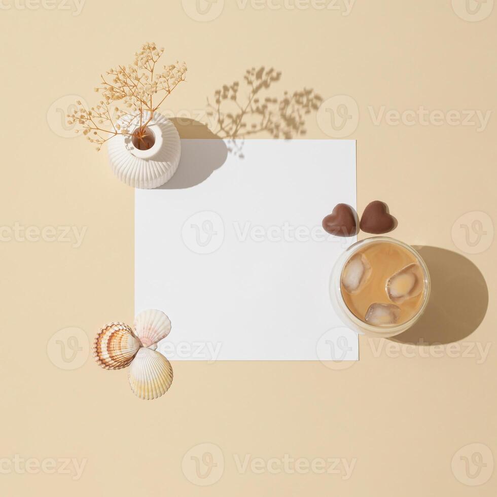 Creative trendy layout made with cup of coffee, chocolate hearts, sea shells, white vase with dry flowers and paper card note copy space on light beige background. Minimal concept. Flat lay. photo