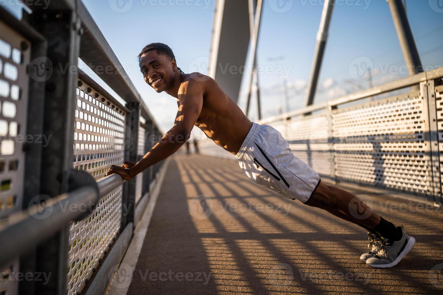 Young african-american man is exercising on the bridge in the city. He is doing push-ups. photo