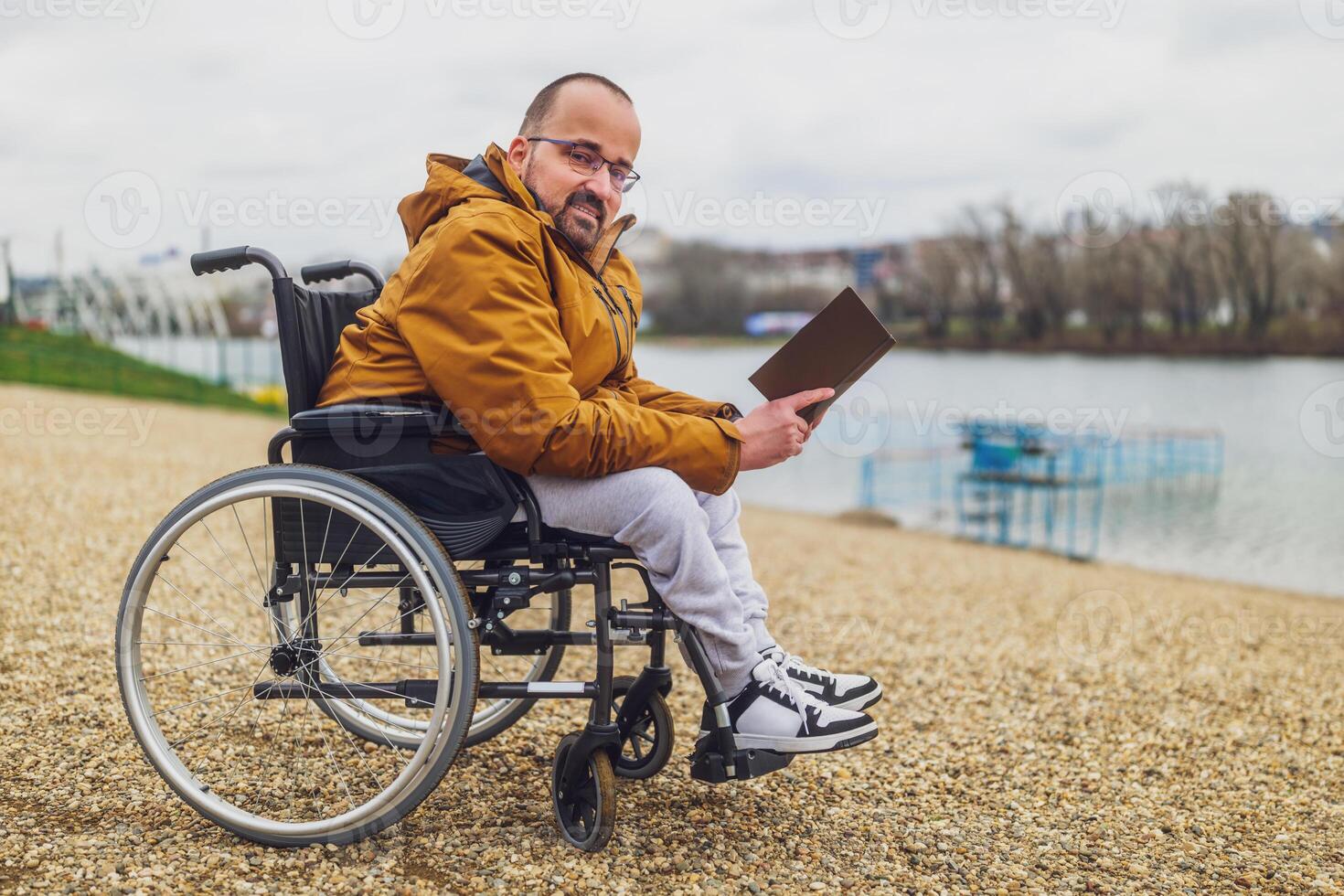 Paraplegic handicapped man in wheelchair is reading book outdoor. photo