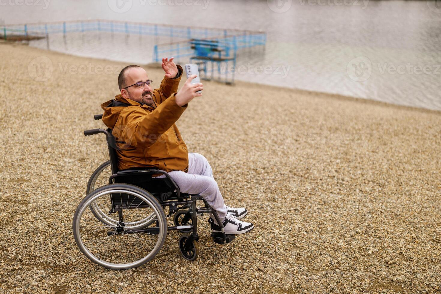 Paraplegic handicapped man in wheelchair is taking selfie with smartphone outdoor. photo