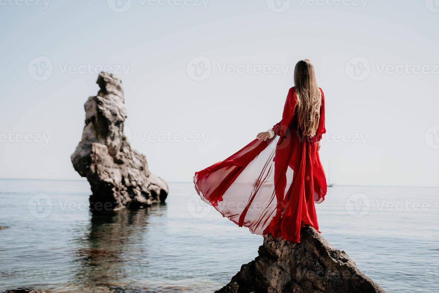 Woman travel sea. Young Happy woman in a long red dress posing on a beach near the sea on background of volcanic rocks, like in Iceland, sharing travel adventure journey photo