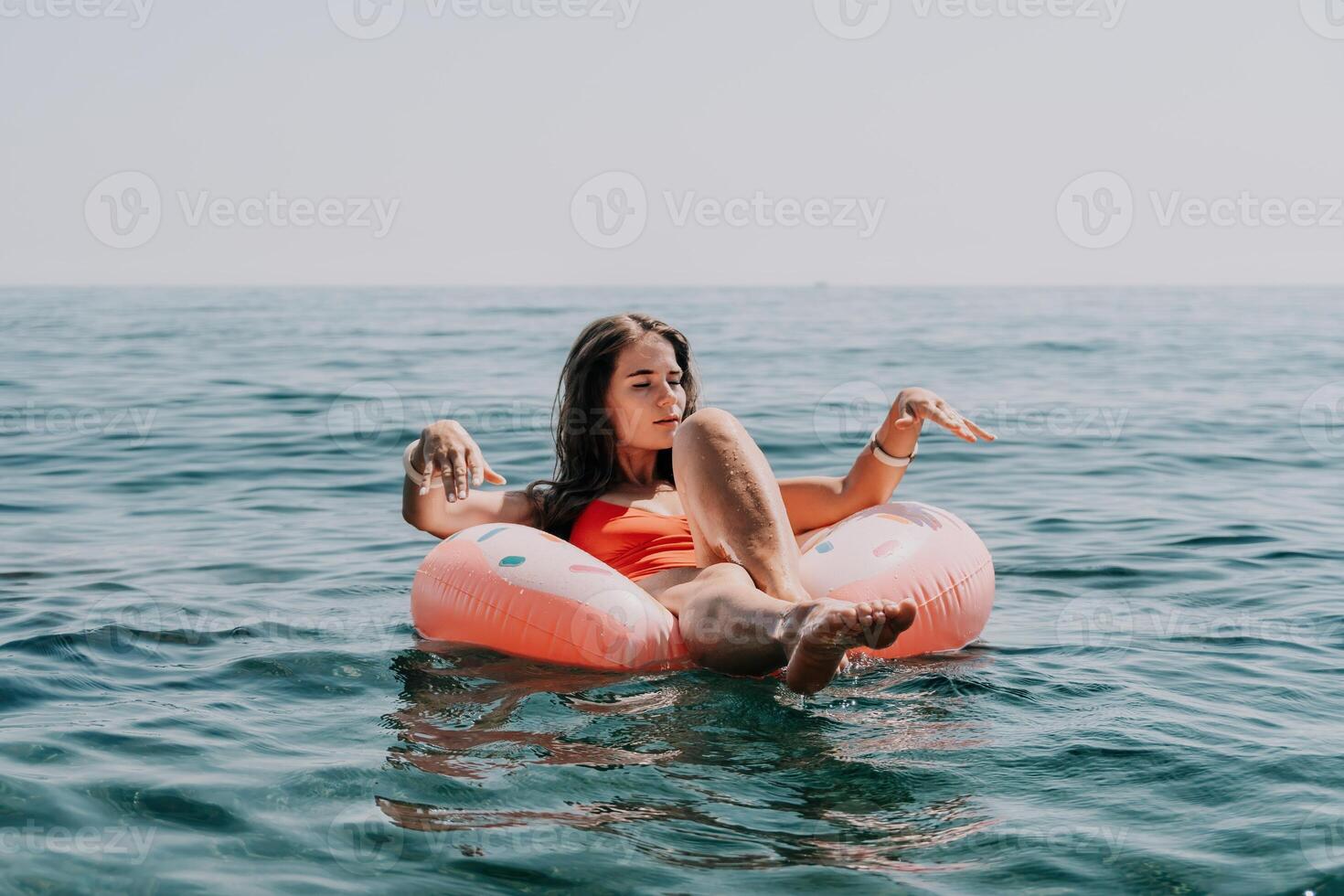 mujer verano mar. contento mujer nadando con inflable rosquilla en el playa en verano soleado día, rodeado por volcánico montañas. verano vacaciones concepto. foto