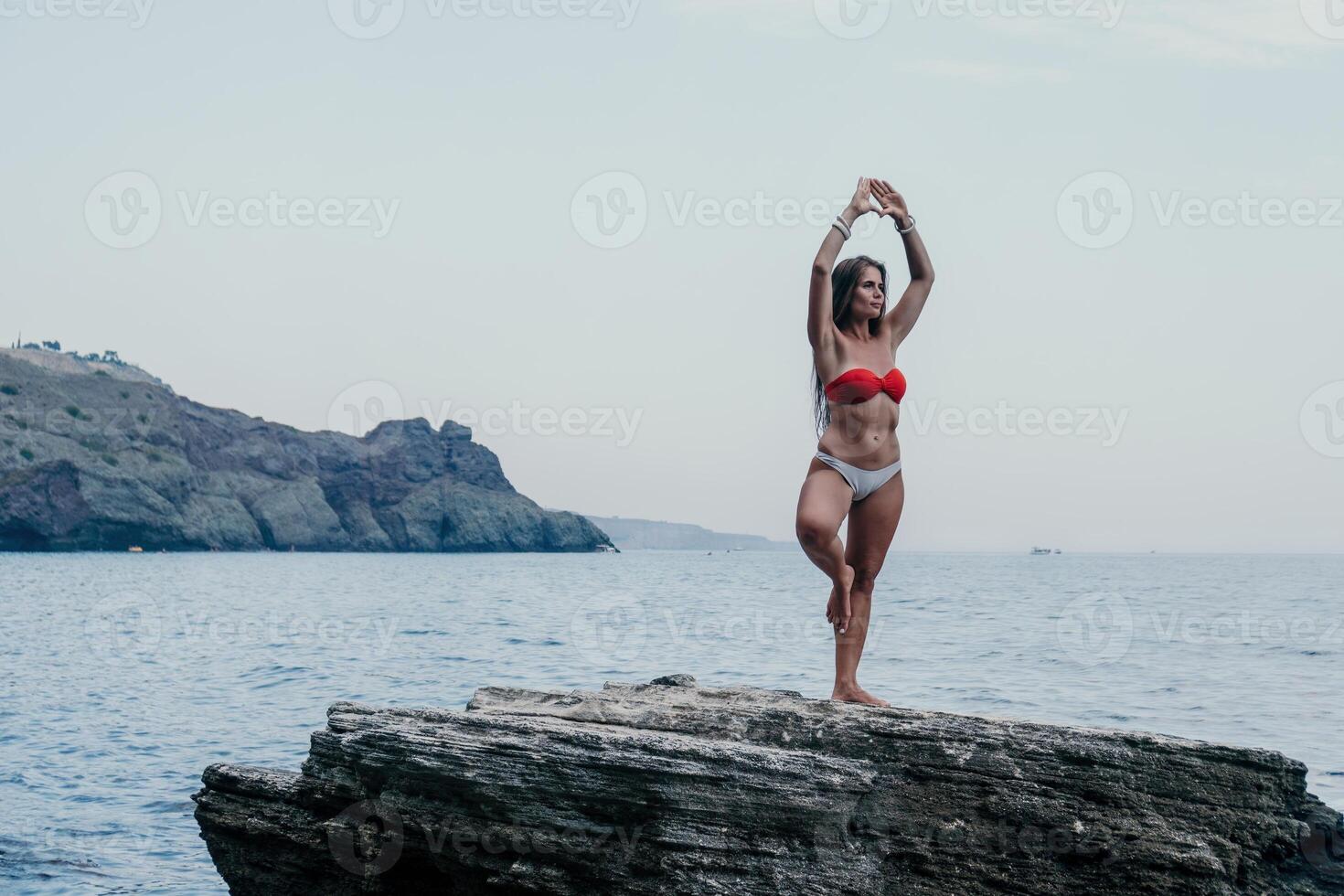 Woman sea yoga. Back view of free calm bliss satisfied woman with long hair standing on top rock with yoga position against of sky by the sea. Healthy lifestyle outdoors in nature, fitness concept. photo