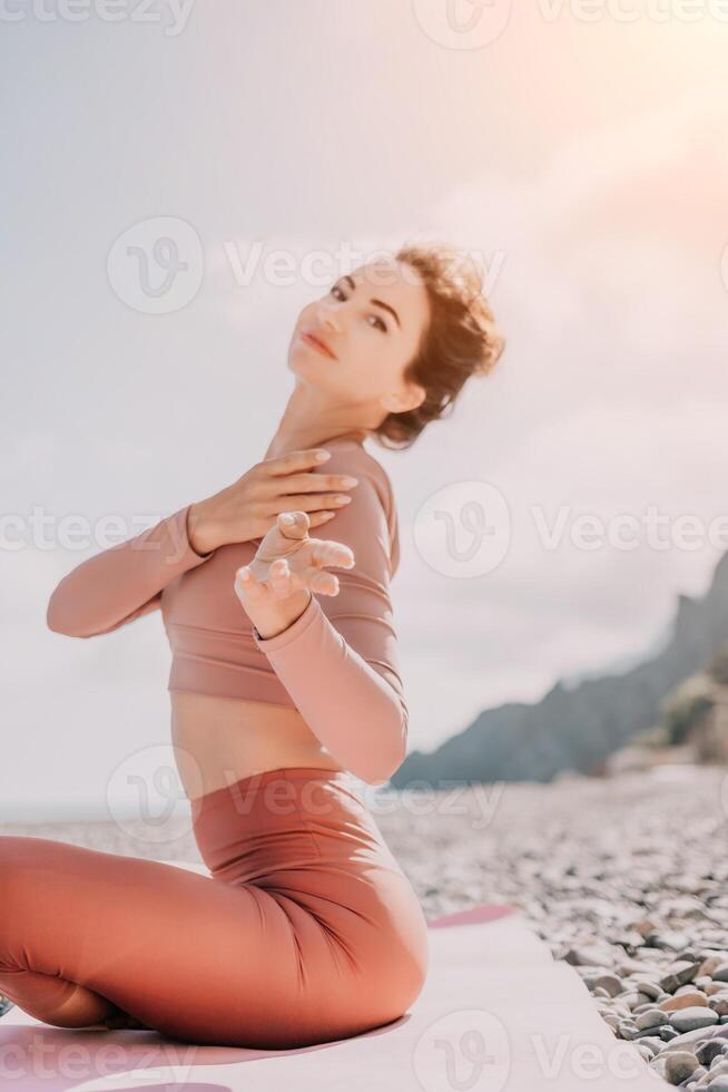 Middle aged well looking woman with black hair, fitness instructor in leggings and tops doing stretching and pilates on yoga mat near the sea. Female fitness yoga routine concept. Healthy lifestyle photo