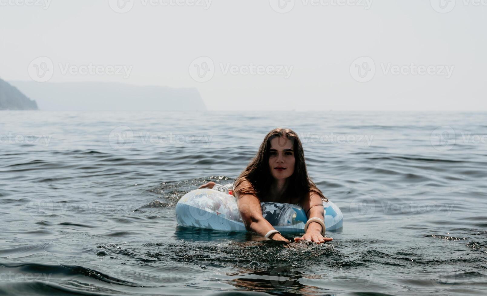 mujer verano mar. contento mujer nadando con inflable rosquilla en el playa en verano soleado día, rodeado por volcánico montañas. verano vacaciones concepto. foto