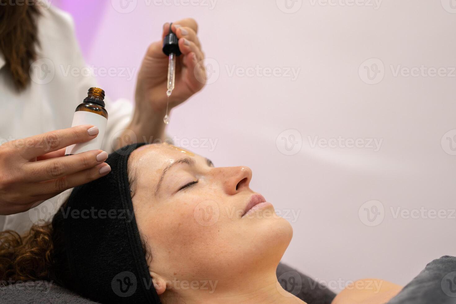 Crop beautician applying serum on client face in beauty salon photo