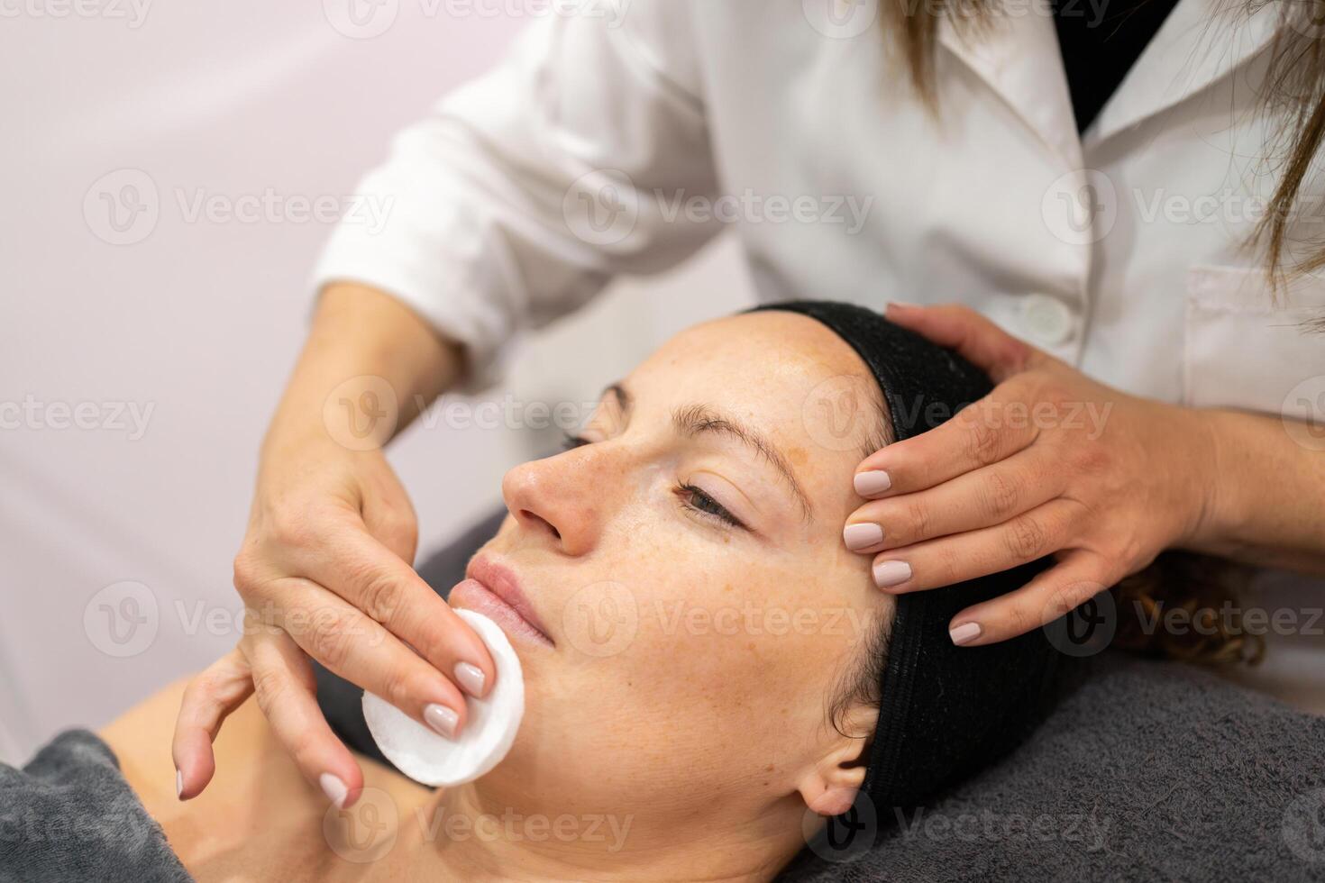 Crop beautician cleaning face of client with skin care cotton pad in beauty salon photo